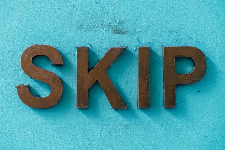 A close-up view of three large, three-dimensional metallic letters spelling 'SKIP' affixed to a vibrant turquoise wall with a textured surface. The brownish-metal letters have a matte finish, with sub