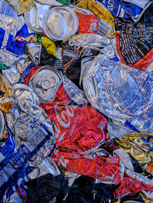 A large outdoor area shows numerous stacks of flattened cardboard boxes with graphics and text indicating they previously contained fresh fruits, arranged in multiple piles. Surrounding the stacks are